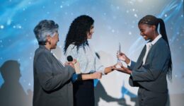 Women, award and happy on conference stage, mic and giving prize for performance at company. Person, staff and trophy at event with thanks, goal and smile for reward with success in finance career