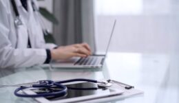 Tablet computer and blue stethoscope are on the glass table while doctor woman is using laptop computer on the glass table. Medicine concept