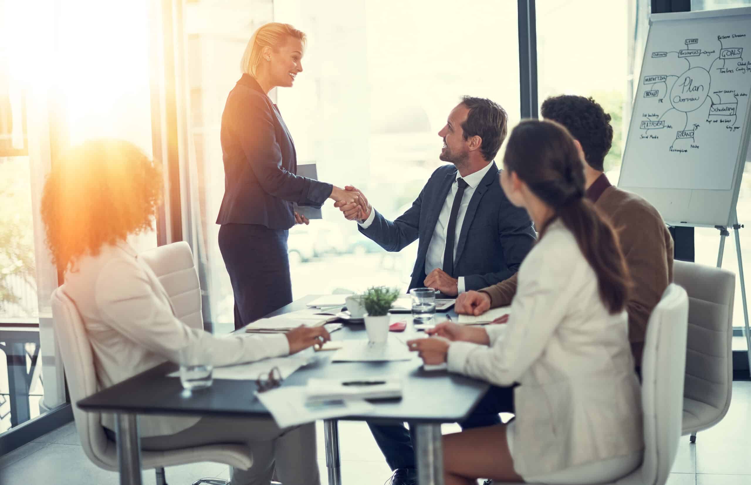 Handshake, success and contract with business people in meeting for deal merger, acquisition and thank you. Teamwork, loan agreement and banking firm with employees in office with lens flare
