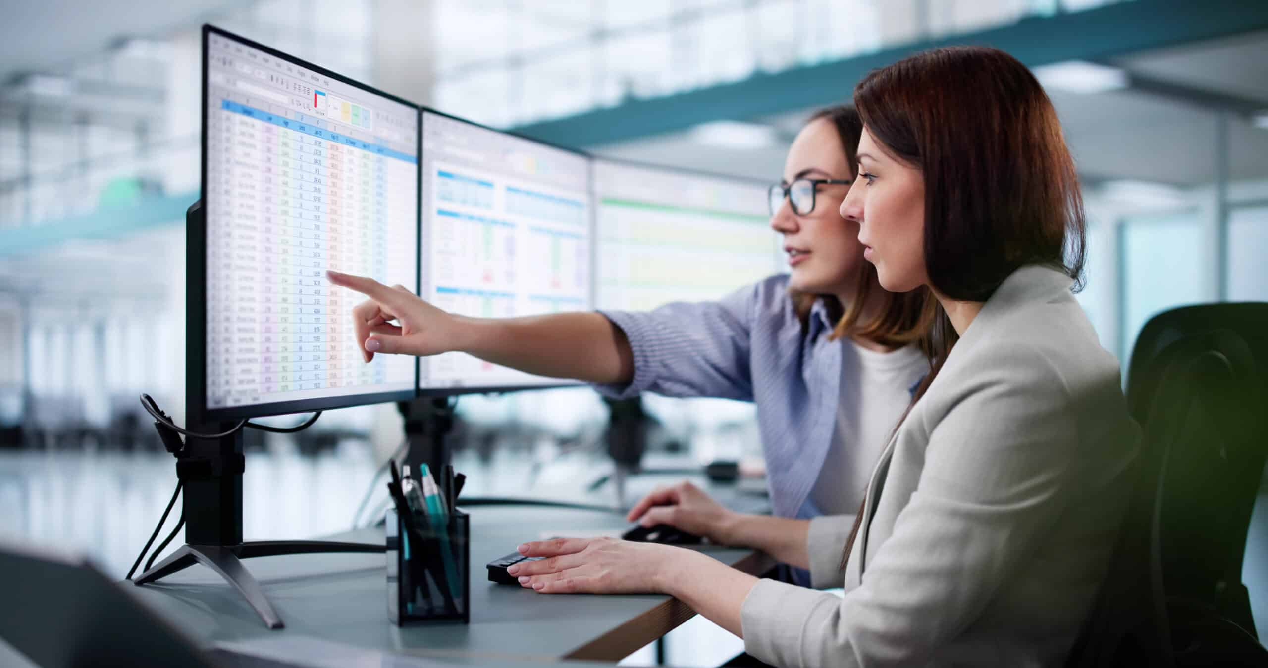 Two professionals analysing data dashboards on dual monitors as part of Prolifics’ data reporting solutions for improved business intelligence reporting