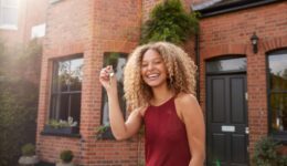 Portrait Of Excited Young Woman Standing Outside New Home Holding Keys