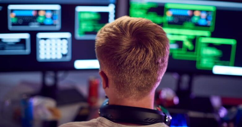 Male Teenage Hacker Sitting In Front Of Computer Screens Bypassing Cyber Security