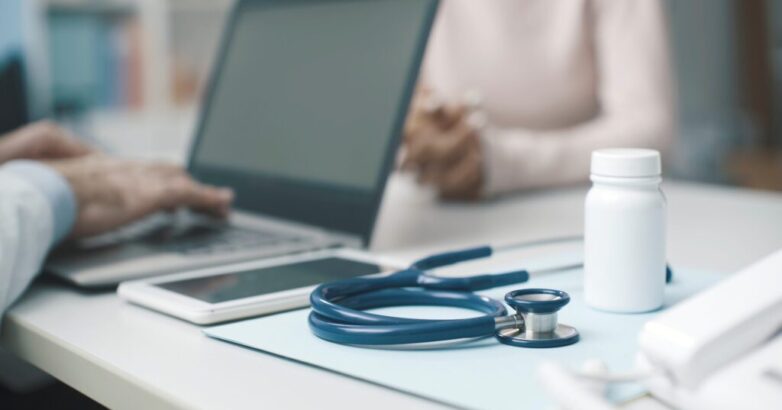 Doctor talking with a patient and typing with his laptop