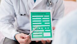 Contemporary doctor in whitecoat pointing at electronic form of health insurance