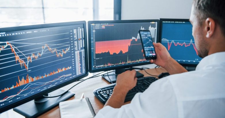 Young businessman in formal clothes is in office with multiple screens. Conception of exchange and money