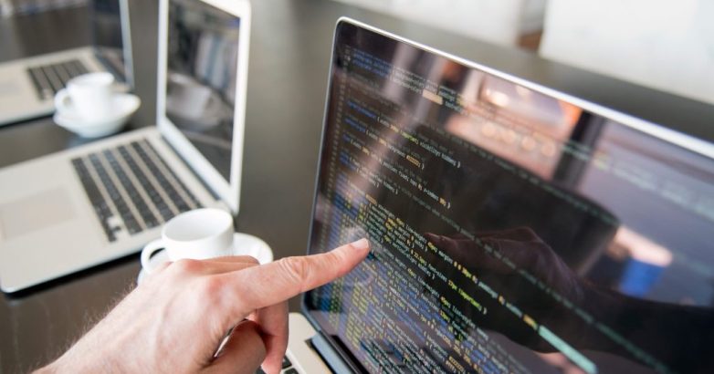 Hand pointing to line of code on computer screen.