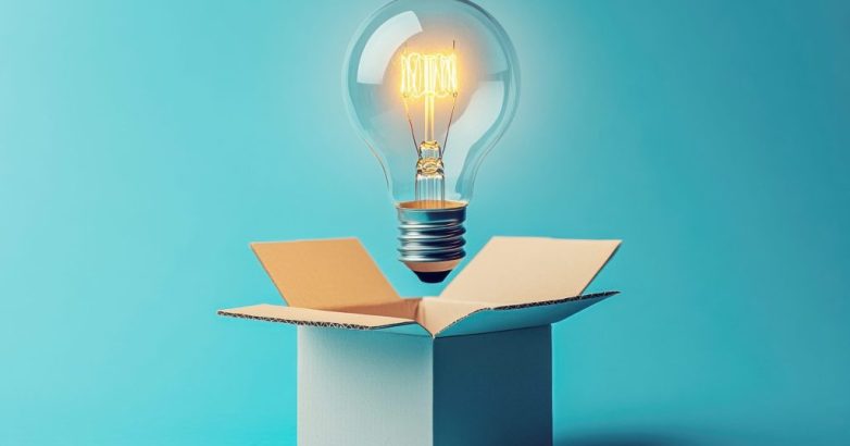 Glowing lightbulb emerging from open white cardboard box against turquoise backdrop, symbolizing breakthrough creativity