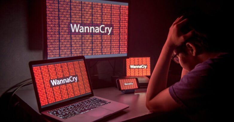 Young Asian male frustrated, confused and headache by WannaCry ransomware attack on desktop screen, notebook and smartphone, cyber attack internet security concept