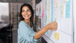 Smiling Latina professional woman placing sticky notes on planning board
