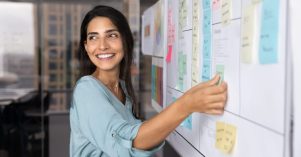 Smiling Latina professional woman placing sticky notes on planning board