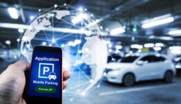Pick me up, mobile smart phone in hand using application for intelligent car park with digital hologram on blurred parking car background, mobile auto parking, network and online technology concept
