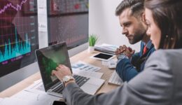 Side view of computer systems analysts using charts on computer monitors while working in office