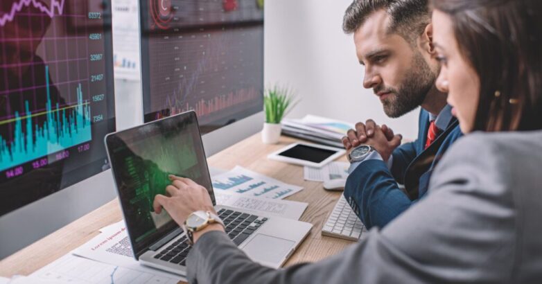 Side view of computer systems analysts using charts on computer monitors while working in office