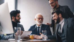 Four businessmen, three young managers and a senior CEO, joking and laughing during an office meeting.