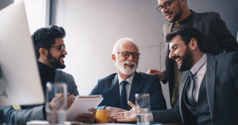 Four businessmen, three young managers and a senior CEO, joking and laughing during an office meeting.