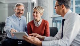 Happy mid adult couple using touchpad with their financial consultant in the office.