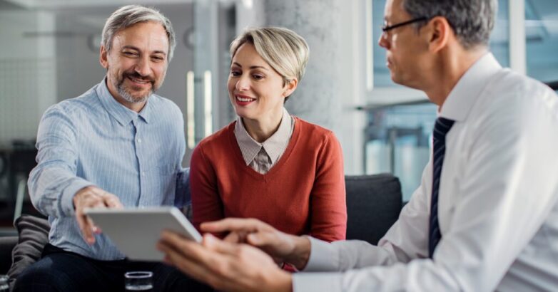 Happy mid adult couple using touchpad with their financial consultant in the office.
