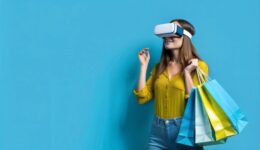 Young woman with shopping bags using virtual reality headset on blue background.