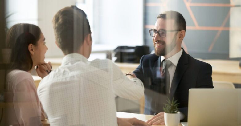 Male realtor handshaking clients after successful negotiations i