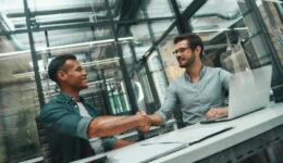 Welcome on board! Two young and handsome men shaking hands and smiling while working in modern office