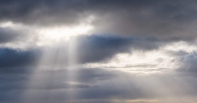 A scenic view of of sunrays shinings through hole of clouds in dusk dramatic sky. Cloudscape sky background.