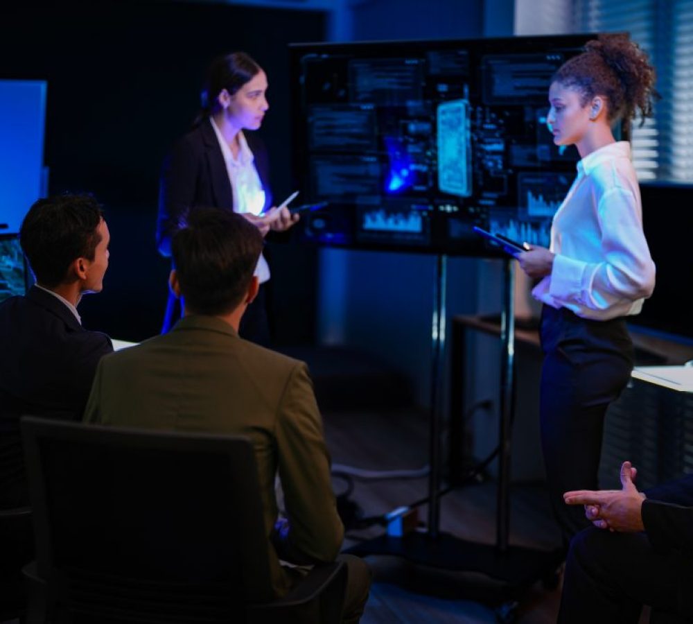Diverse corporate business team planning global market strategy in late night shift office. Female leader presenting investment project on smart digital screen dashboard.